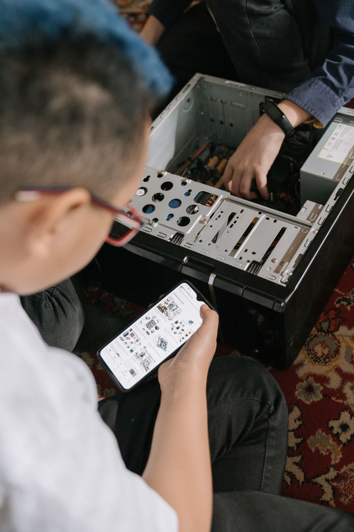 Services Two individuals fixing a computer while using a smartphone for repair guidance.