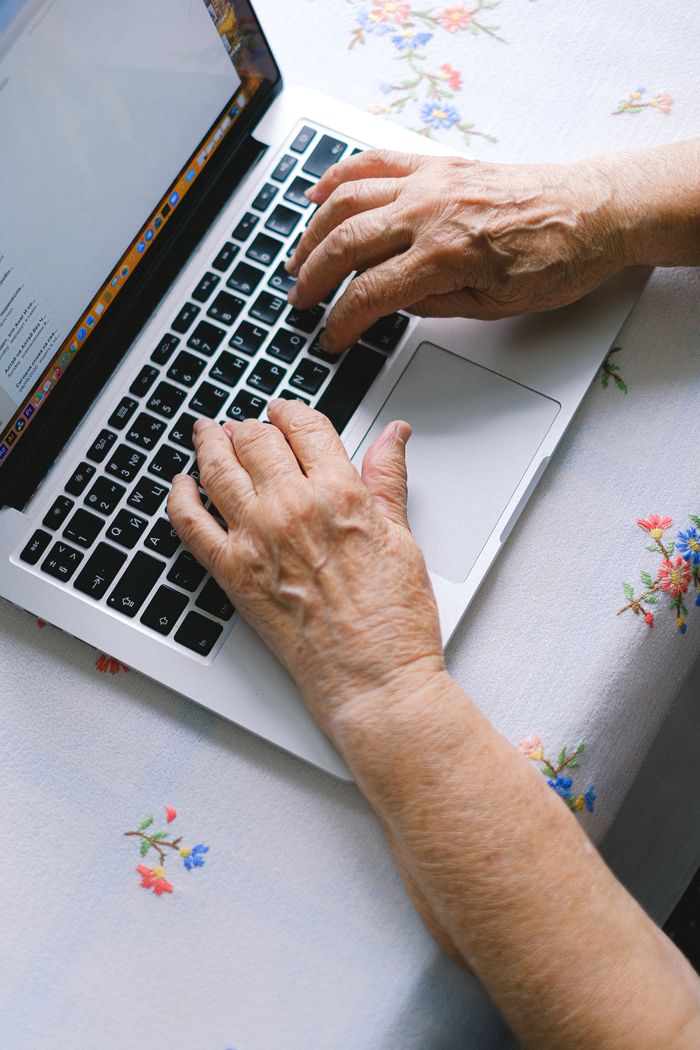 Services Elderly hands typing on a laptop keyboard at home, promoting digital literacy among senior adults.
