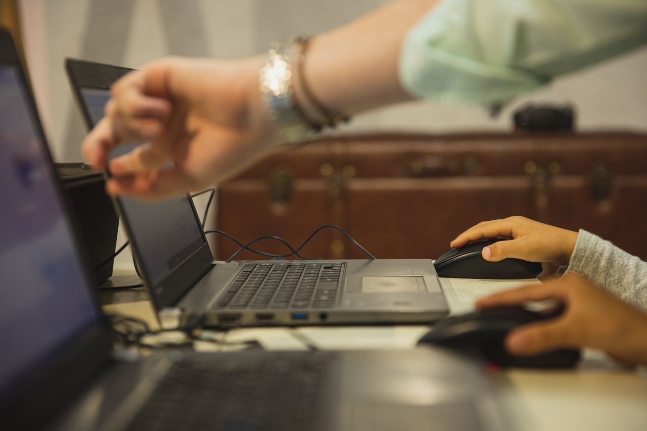 Services Crop anonymous female teacher pointing at netbook screen near schoolchildren touching mouses at desk in classroom